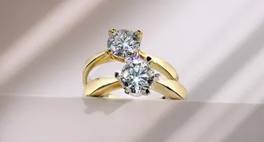 Dwa złote pierścionki z okrągłymi diamentami na jasnym tle.